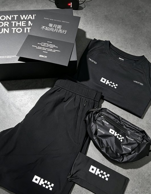 A flat lay photo displays black athletic apparel including shorts, a t-shirt, and a crossbody bag, all branded with the 'OKX' logo, along with a black box featuring Chinese text and the OKX logo.