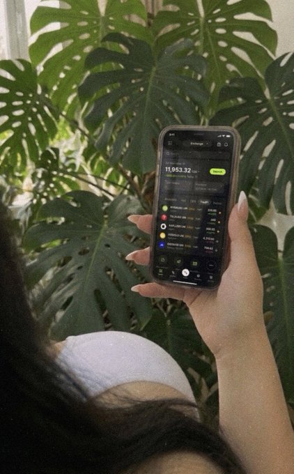 The image shows a person holding an iPhone next to a large green plant, possibly displaying some information about cryptocurrency exchanges or crypto news. One of the text items from this image reads "quietly, X-Perps became one of crypto' s fastest-growing products $30.7B weekly volume by the end of Q1." It seems like the person might be researching or learning more about crypto markets and exchanges.