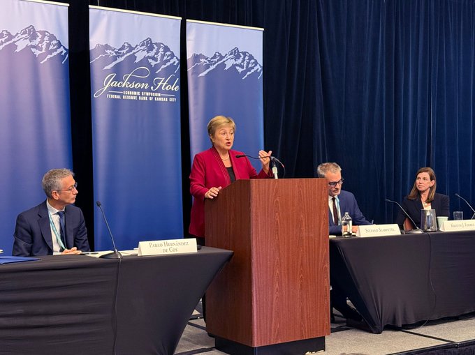 A woman in a red blazer speaks at a podium during a panel discussion at the Jackson Hole Economic Symposium, with name placards visible for "Pablo Hernández de Cos" and "Kristin Forbes" seated at the table. The image accompanies a post discussing tokenization in finance and the need for international regulatory coordination, featuring the same speakers mentioned in the tweet.