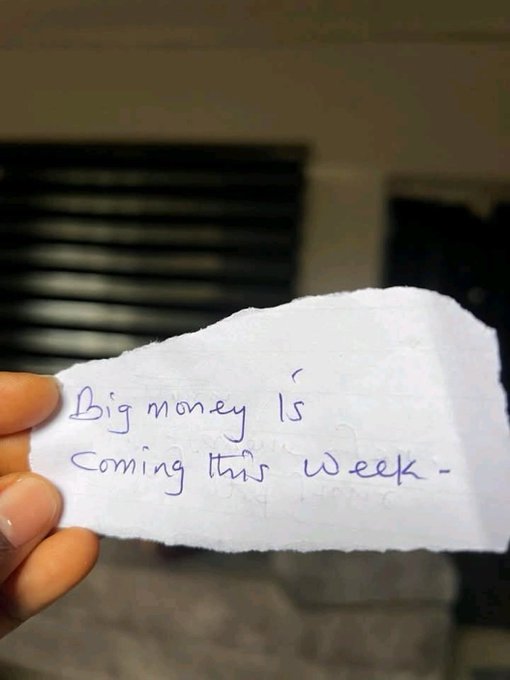 A hand holds up a torn piece of paper with the handwritten note "Big money is coming this week," visually representing the optimistic message about manifesting financial abundance.
