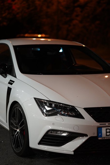 The front end of a white SEAT sports car (Cupra model) photographed at night, showing its distinctive headlights and grille.