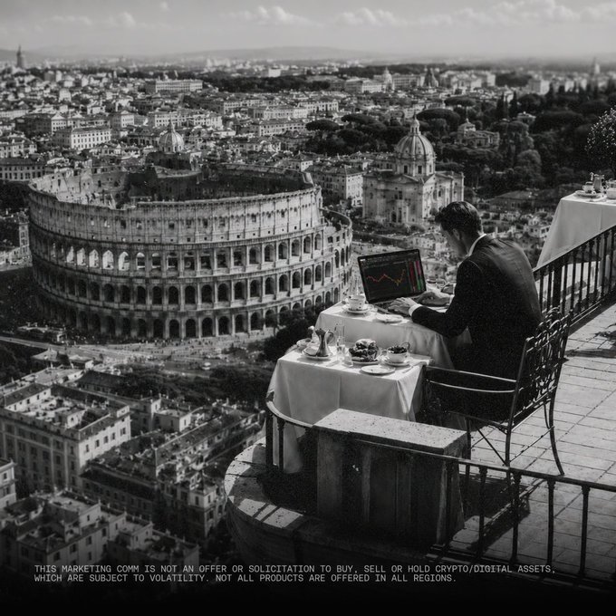 Black and white image showing a man in a suit working on a laptop at a dining table set on a balcony overlooking the Colosseum in Rome, with a disclaimer reading 'THIS MARKETING COMM IS NOT AN OFFER OR SOLICITATION TO BUY, SELL OR HOLD CRYPTO/DIGITAL ASSETS. WHICH ARE SUBJECT TO VOLATILITY. NOT ALL PRODUCTS ARE OFFERED IN ALL REGIONS.'