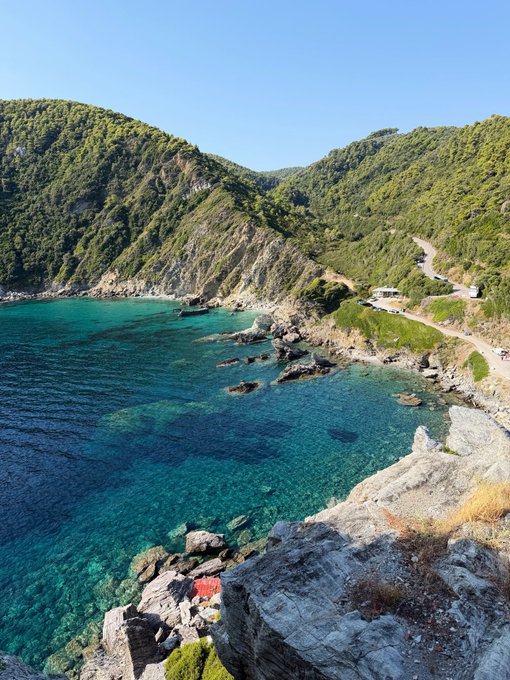 A breathtaking coastal scene featuring turquoise waters nestled between lush, green hillsides, with a winding road snaking along the cliffs. There is no visible text, numbers, or names in the image, though its serene, untouched beauty evokes the same sense of calculated discovery and conviction that the post describes when entering the PONS position.