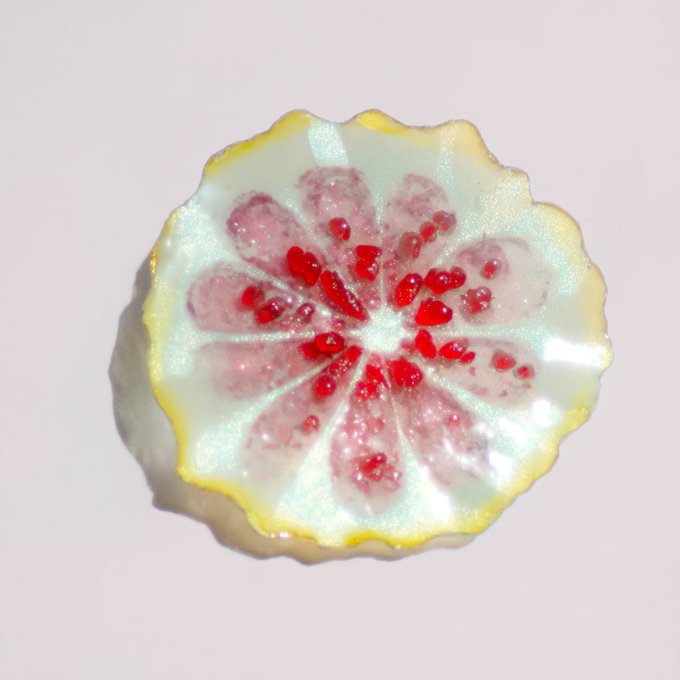 A close-up of a decorative flower-shaped candy or chocolate with red details resembling seeds, encased in a clear, yellow-edged disc.