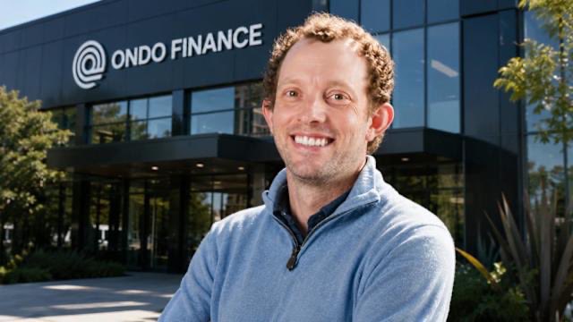 The image features a man standing outside of an office building that has the name "Ondo Finance" written on its facade. The man appears to be smiling for the camera, possibly posing for a photo or attending an event at the company's location. In the background, there are some potted plants and trees, adding greenery to the scene. The image also contains text that reads: "We are deeply saddened to hear the passing of a pioneer in web3 Nathan Allman founder of @OndoFinance, a leader in RWAs. Has unexpectedly passed away. Our condolences and hearts are with his family and team at Ondo May he Rest in Peace". This message is related to the man standing outside the office building, as it seems that he might have been involved in or connected to Nathan Allman's work in web3 technology.