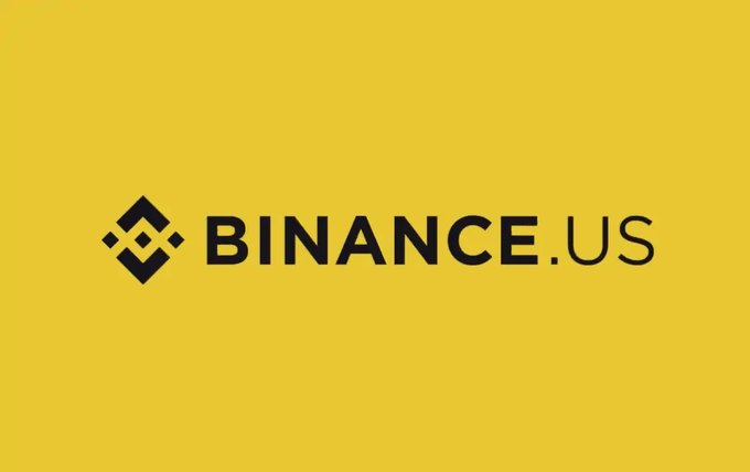 The image displays the Binance.US logo, featuring a black diamond-shaped icon next to the text "BINANCE.US" on a yellow background. This logo directly relates to the news of BinanceUS seeking a CFTC license to launch prediction markets under CEO Steven McWhirter.