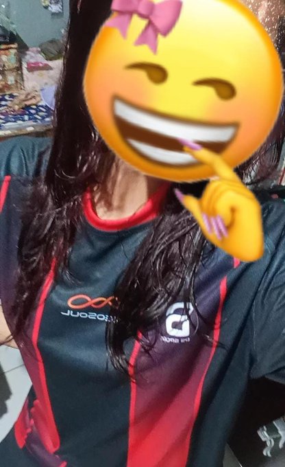 A person with long dark hair takes a selfie wearing a black and red "iZugar" and "NeoSoul" Web3 jersey, with their face obscured by a smiling emoji with a pink bow. The image captures the excitement of receiving their first Web3 jersey after joining the cheerleader event.