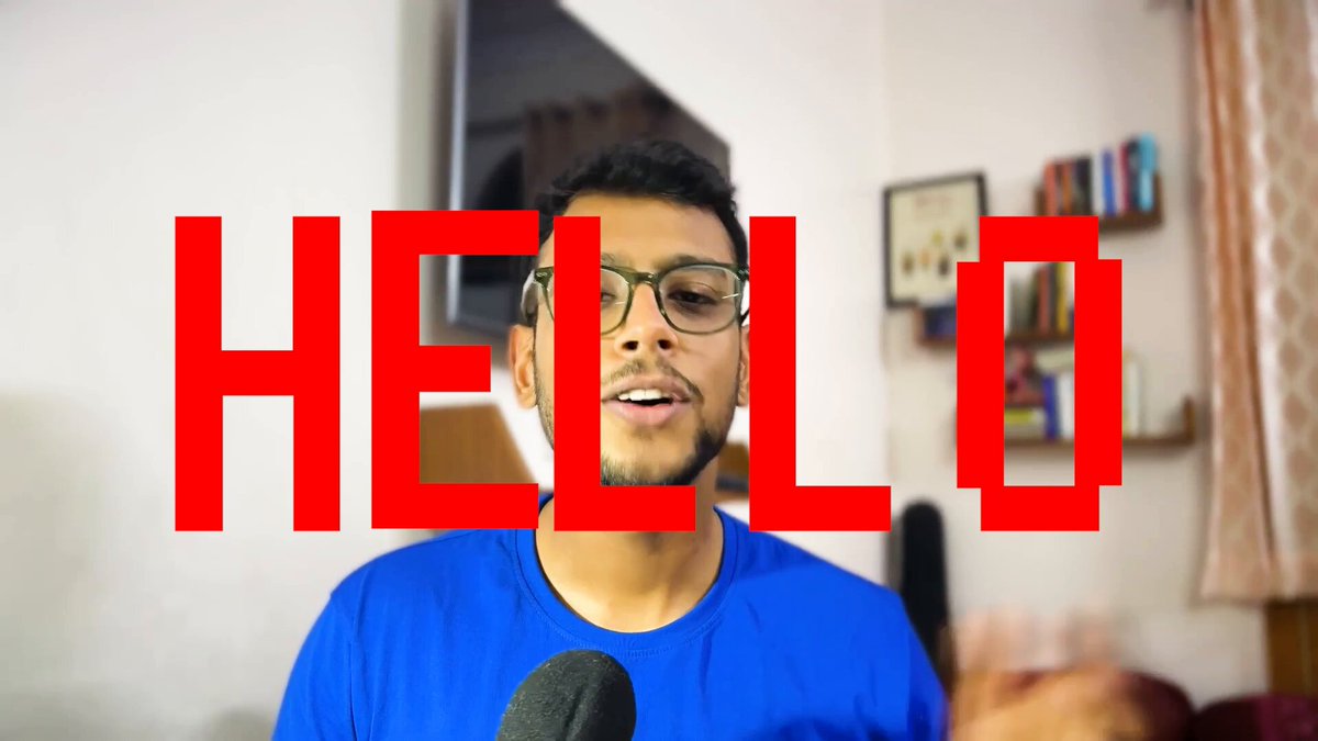 The image features a man wearing glasses standing against a white wall while using an infrared video camera, possibly for recording himself speaking into or discussing the contents of the Hello word. The surrounding environment suggests that he might be in a living room setting with a bed visible behind him and numerous books on shelves nearby.
