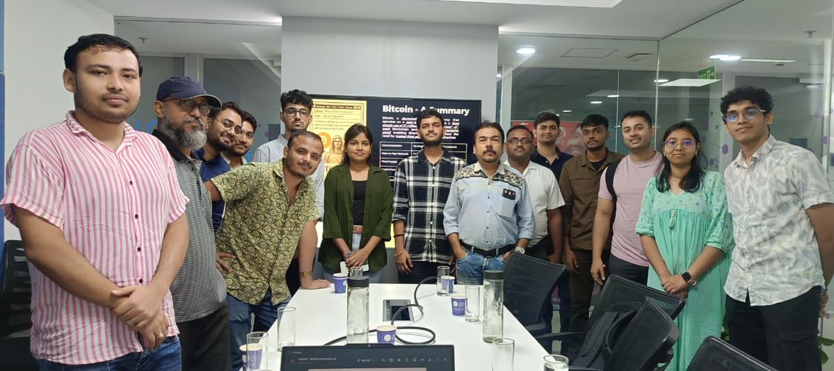 A group of attendees poses together at the "Bitcoin 101: How Digital Money Works Without Banks" meetup, with a presentation board displaying a "Bitcoin - Summary" visible in the background, reflecting the event's educational focus on Bitcoin.