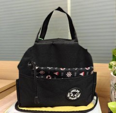 A black canvas tote/lunch bag with a patterned fabric trim and circular logo on a wooden surface.