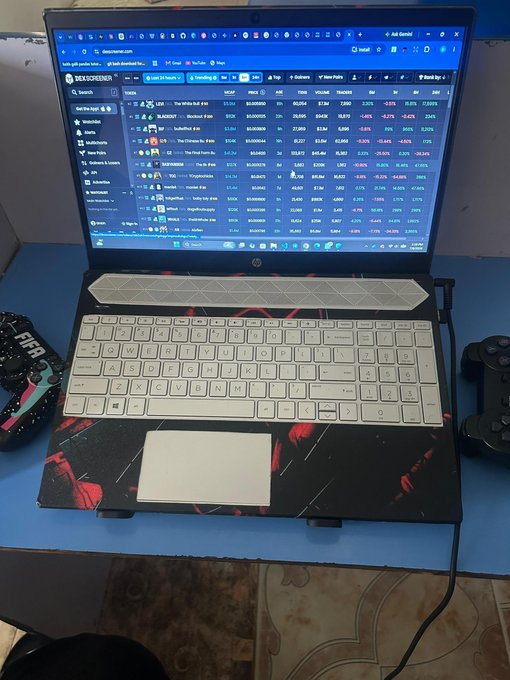 A laptop displays DEX Screener with various Solana memecoins showing red price action, including tickers like RANKO, Inbred, and others, paired with a "FREE RANGE" mousepad and a PlayStation controller—capturing the creator's evening crypto trading routine before logging off for the night.