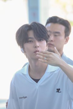 A young man with dark hair blows a kiss toward the camera, wearing a white polo shirt with "courtage" and a star logo visible, matching the post's caption about #ALD1 member #허씬롱 #贺鑫隆 (#XINLONG) at ICN Airport on 260812.