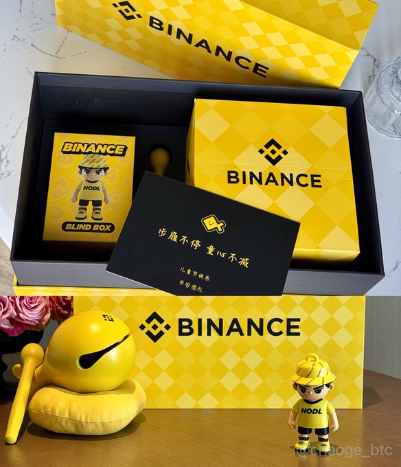 The image features a yellow binance box with a toy figure of a boy wearing a hat, sitting next to it. The box also contains a card that has Chinese characters on it. The post includes information about binance and a link to a website called hopecanagement.bc.