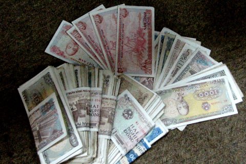 A fan of various international banknotes spread out on a dark surface, featuring multiple currencies including Vietnamese dong and Chinese yuan denominations.