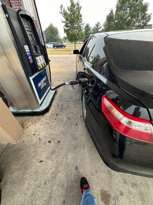 A black car refueling at a Murphy USA gas pump, with the photographer's feet visible at the bottom of the frame.