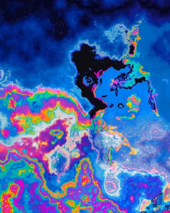 A vibrant, psychedelic abstract artwork with swirling blues, purples, pinks, greens, and yellows creating a marbled, cosmic-like effect with dark cloud-like formations in the upper portion.
