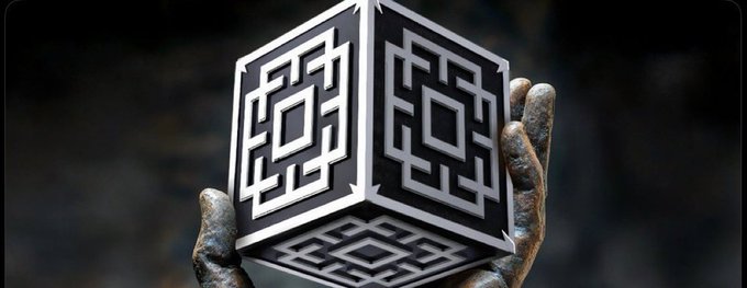 A 3D rendering of a metallic cube with a QR-code-like maze pattern on its visible faces, being held by weathered, mechanical-looking hands.