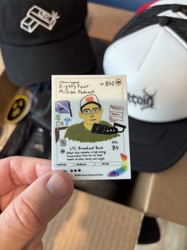 In the image, a person's hand is holding up an item that appears to be a sticker or card featuring a cartoon of a man wearing a hat with the words "Bitch" written on it. The background of the image shows a box containing more stickers and cards. The caption below the image reads "The 84 Million Shop goes to Amsterdam... See y'all soon, EU fam! eightyfourmillion.com/shop #packing #ltc". This suggests that the person holding up the item is likely promoting or selling these items online, possibly targeting a niche audience interested in merchandise related to the "Bitch" subculture.
