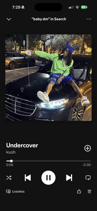 A Spotify screenshot playing the song 'Undercover' by kush, searched for as "baby dm", with the album art showing a person in a green hoodie sitting on a Mercedes-Benz.