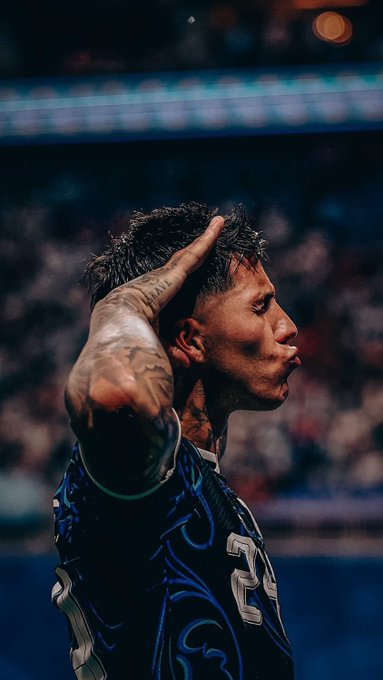 A profile shot of a tattooed soccer/football player in a dark blue jersey with the number 23, raising his hand to his head in a stadium setting.