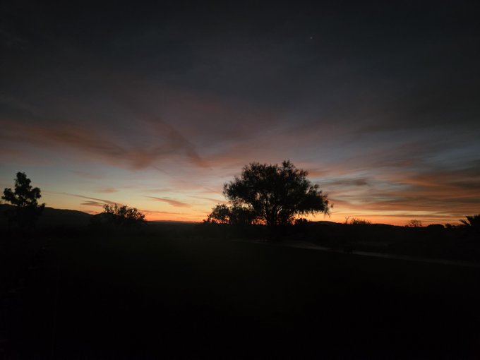 A scenic photograph of a sunset with vibrant orange, pink, and purple clouds silhouetting trees and a landscape in the foreground.