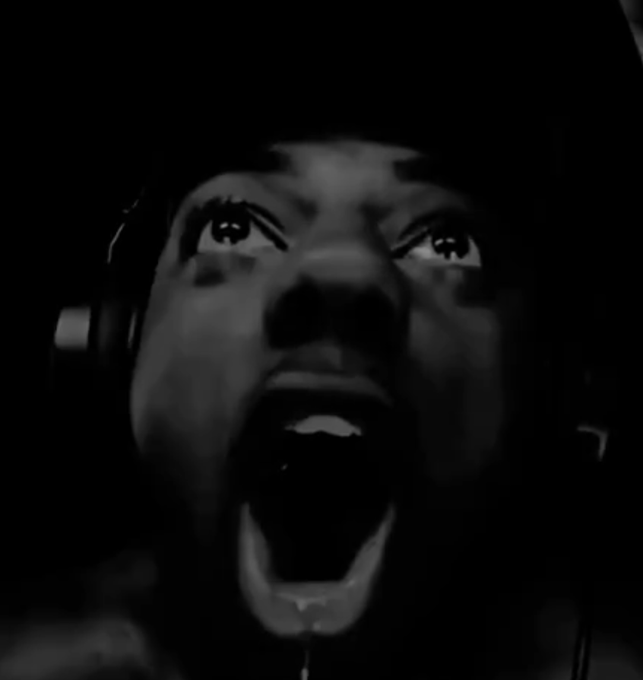 A dramatic black-and-white close-up of a person's face screaming or singing passionately, wearing headphones in a dark setting.