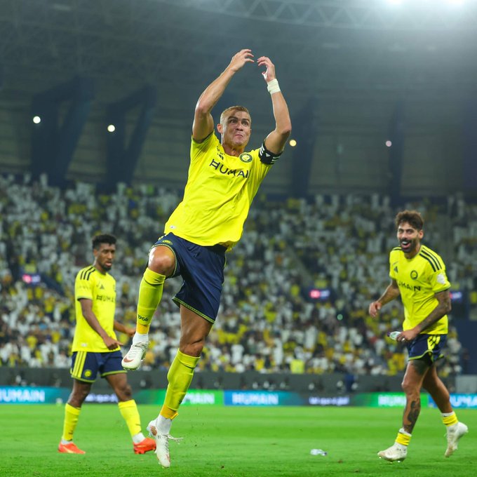 A soccer player in a yellow "HUMAN" jersey leaps in celebration after scoring, with two teammates in matching kits running toward him in a packed stadium. The image reflects the post's message about consistent contribution and meaningful attention, capturing a moment of dedicated effort paying off on the field.