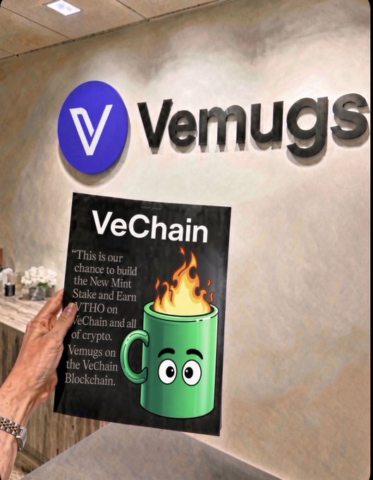 A hand holding a VeChain (Vemugs) promotional poster in front of a Vemugs wall sign, advertising 'VeChain' as a 'New Mint Stake and Earn VTHO' opportunity on the VeChain Blockchain, featuring a cartoon green mug character.