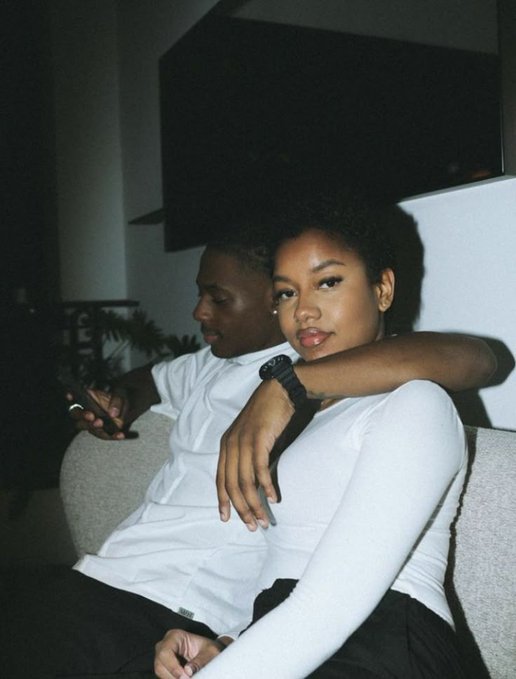 A man and woman sit closely together on a couch at night, the man wearing a white shirt and black watch with his arm around the woman in a white long-sleeve top as she gazes at the camera. The intimate, relaxed pose reflects the post's nostalgic tone about a memorable day shared together.
