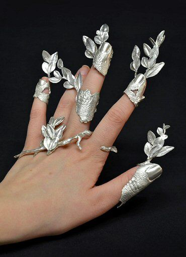 A hand wearing elaborate silver jewelry designed to look like leafy vines, branches, and flowers covering the fingers as ornate rings and armor.