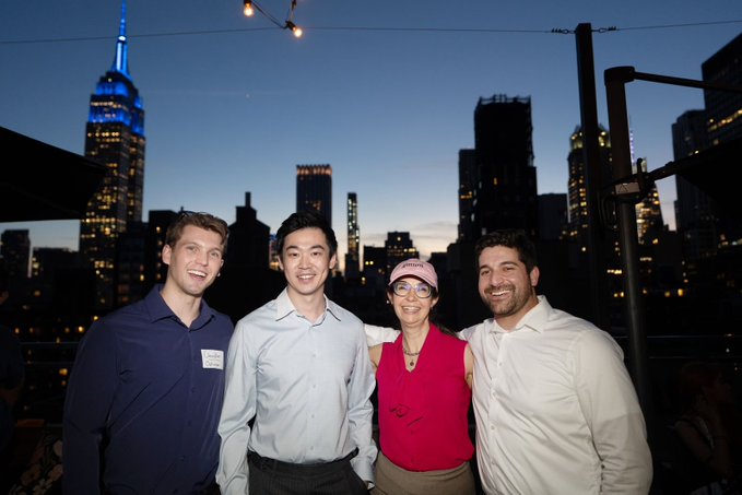 The image features a group of four people posing for a photo, standing together with smiles on their faces. They are all dressed up and appear to be enjoying themselves. The backdrop of the photo includes a city skyline at night, which adds an interesting contrast between the urban setting and the group's gathering. The caption provided in the image seems to be related to a recent event or party they attended, possibly featuring a discussion about cryptocurrency or financial markets.
