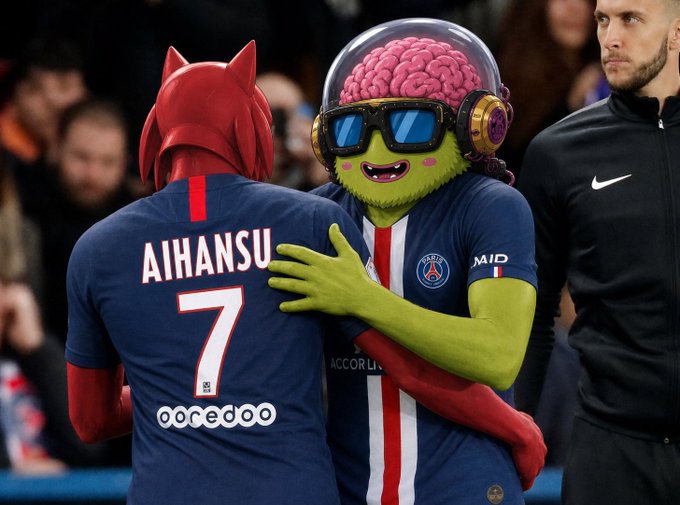 A humorous edited image showing two soccer players embracing, with one wearing a dark blue jersey labeled 'AIHANSU 7' (similar to PSG kits) and the other replaced with a green alien character wearing a brain dome and sunglasses, while a referee stands in the background.