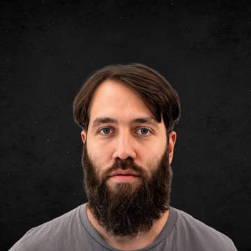 A portrait of a man with brown hair and a full beard wearing a gray shirt against a dark background.