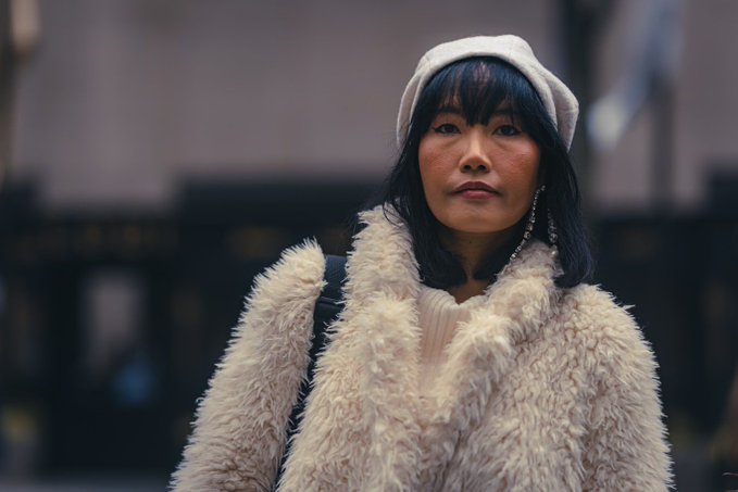 A street-style portrait of a woman with dark hair and bangs wearing a fluffy cream-colored coat and a white beret.