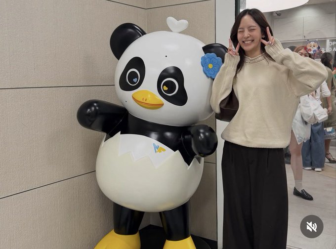 A smiling woman poses playfully with Luna, the panda mascot of the Korean ice cream brand Baekseol (appearing to hatch from an egg), with the partially visible text "OP" and "A" in the background, capturing a cheerful fan moment.