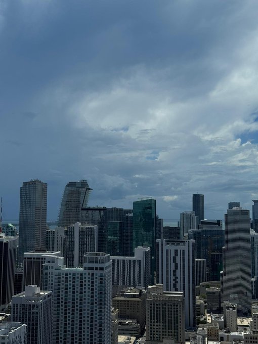 An elevated view of a dense city skyline featuring numerous high-rise buildings under a partly cloudy blue sky.