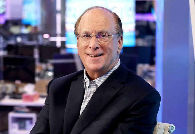 A smiling older man in a dark blazer and checked shirt, wearing glasses, sits in what appears to be a busy newsroom or broadcast studio setting. The accompanying post discusses BlackRock and Ripple's RLUSD tokenized Treasuries, suggesting a connection to the figure shown, though no identifying text or logos are visible in the image itself.
