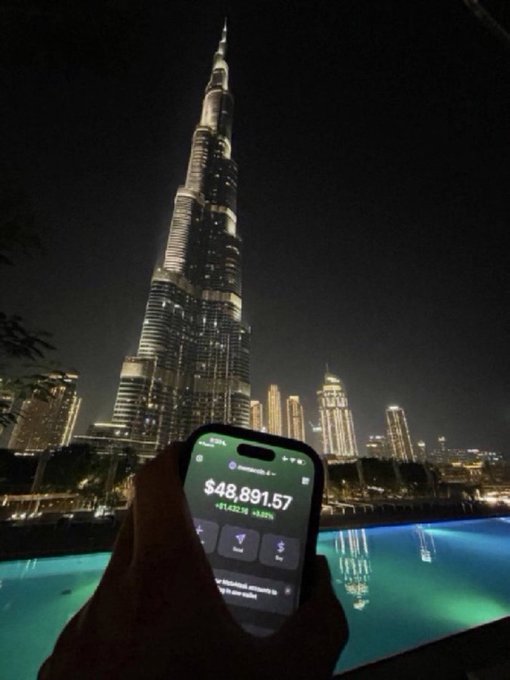 A hand holds a smartphone displaying a Solana wallet balance of $48,891.57 (+$1,432.16) in front of the illuminated Burj Khalifa at night, tying into the post's call to share SOL addresses. The juxtaposition of a crypto portfolio screenshot against the iconic Dubai skyscraper visually showcases a successful crypto earnings achievement.