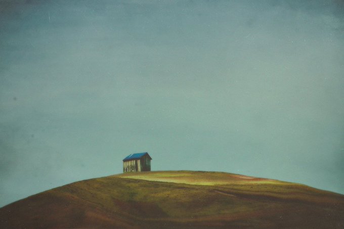 A small, isolated house with a blue roof sits on top of a brown and green hill under a vast, gradient blue sky in this minimalist painting.