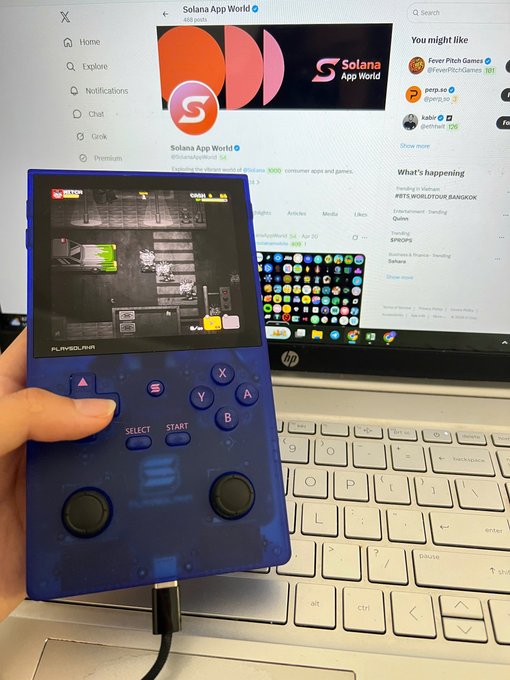 The image shows a person holding a blue game controller with two buttons and a power cord plugged into an open laptop computer. The laptop screen displays a website called "PSG1 Game Spotlight" along with other information about the game, such as its title, release date, and gameplay details.