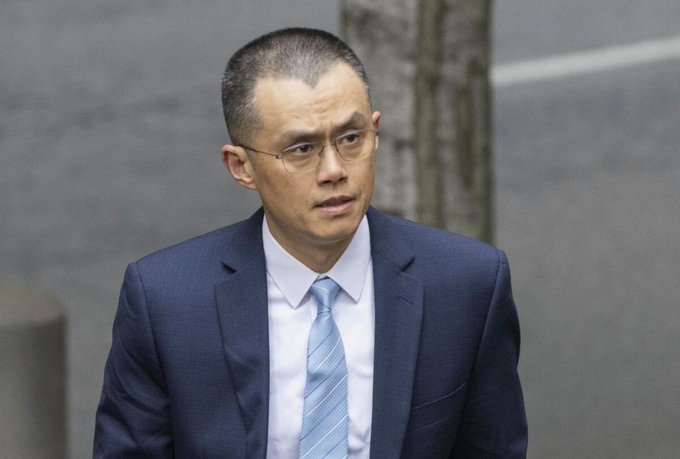 A man with a buzz cut, wearing a dark blue suit, white dress shirt, and light blue striped tie, walks with a serious expression. The image accompanies a quote from Binance founder Changpeng Zhao (CZ) discussing potential bear market conditions amid abundant investment capital.