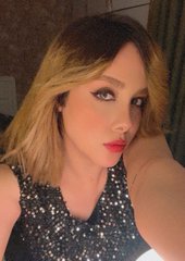 A selfie of a blonde woman with red lipstick wearing a sparkly black top in a dimly lit indoor setting.