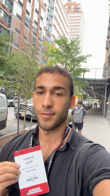 Man taking a selfie outside holding a 'Channel' lanyard badge reading 'Benny Drama' and 'NEW YORK X DMZ'.
