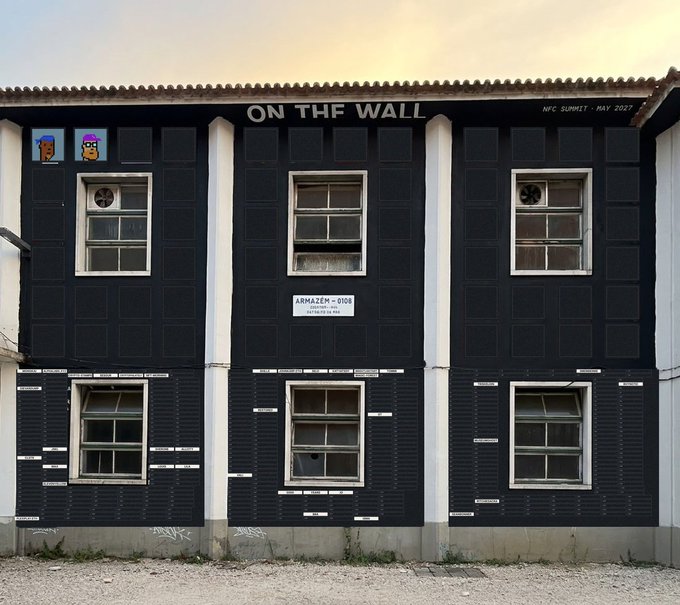 A two-story building with a black facade and white trim displays the text "ON THE WALL" and "NFC SUMMIT - MAY 2027", with pixel art characters resembling Travis Scott visible on the upper left corner.