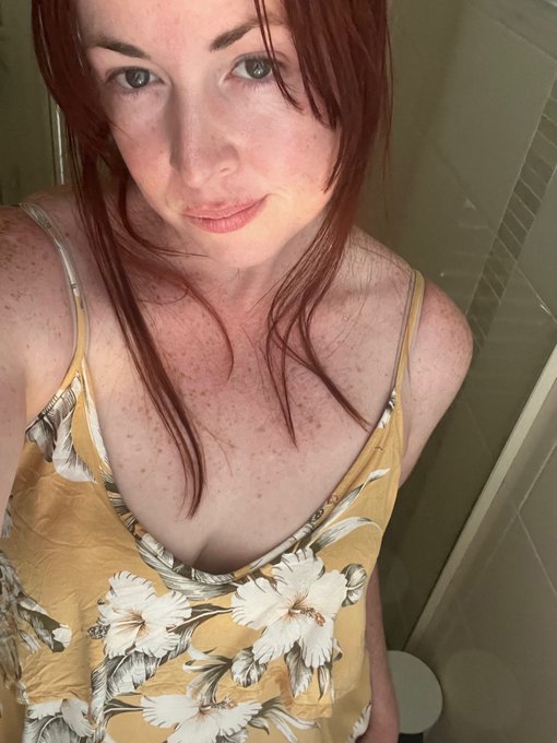 A selfie of a young woman with red hair, freckles, and a yellow floral dress.