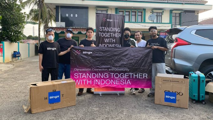 A group of seven people pose together outdoors holding a "Bingx Charity" banner reading "Standing Together with Indonesia," surrounded by Bingx-branded boxes and luggage. The image reflects the post's message of community support, showing a charity team mobilizing aid for those in need across Jakarta.