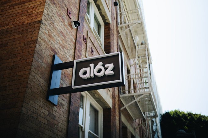 A sign reading "a16z" is mounted on the exterior of a brick building, referencing the venture capital firm mentioned in the post. The image visually anchors the caption's discussion of a16z's commentary on TradFi's interest in blockchain infrastructure over decentralized finance.