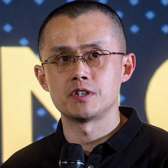 A man with glasses and a shaved head speaks into a microphone against a yellow backdrop with partial text visible behind him. The image appears to show Changpeng Zhao (CZ), the Binance founder referenced in the post about a potential 2026 crypto supercycle.