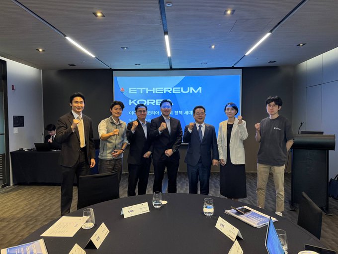 Seven people pose for a group photo in front of a screen reading 'ETHEREUM KOREA 이더리움 코리아 워크샵 세미...'; a man on the far right is Vitalik Buterin.