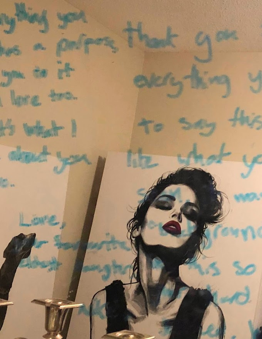 A portrait of a woman with dark hair and red lipstick is displayed on a wall covered in blue handwritten text, including phrases like "that you," "everything," "to say this," and "Love," creating an intimate, introspective atmosphere that mirrors the post's reflection on the unseen struggles of those working hard just to survive.